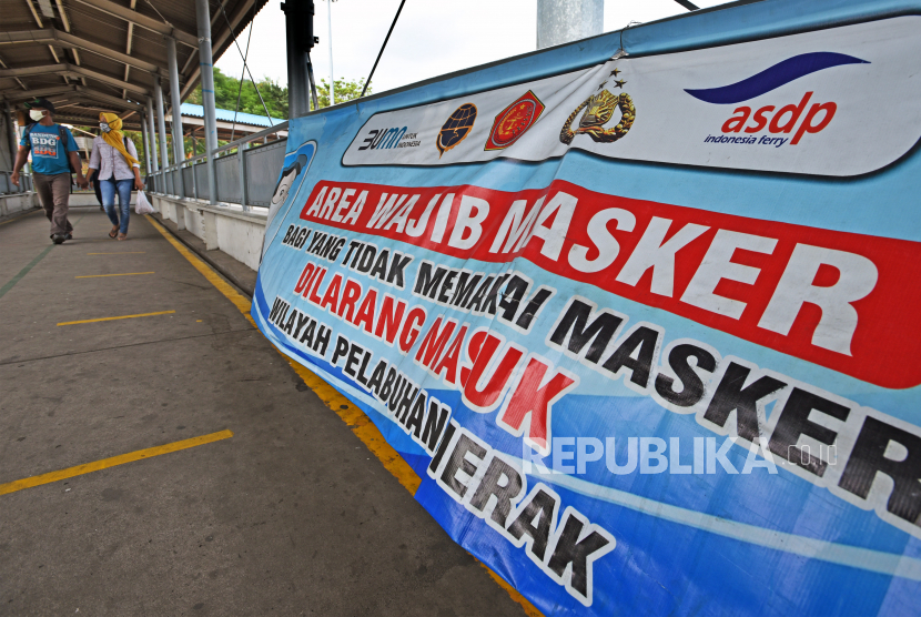 Calon penumpang tujuan Sumatera melintas dekat spanduk area wajib masker di  Pelabuhan Merak, Banten.