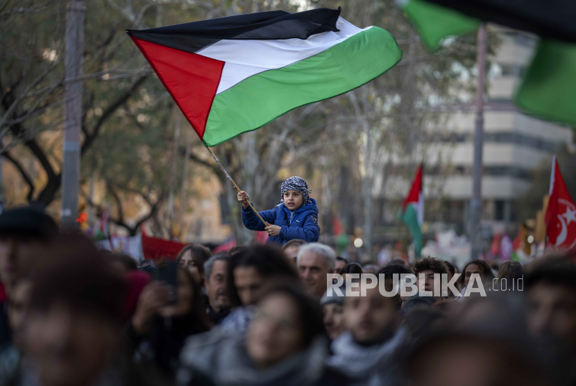 Seorang anak laki-laki mengibarkan bendera Palestina saat para demonstran berbaris dalam protes mendukung warga Palestina dan menyerukan gencatan senjata segera di Gaza, di Barcelona, ​​Spanyol. 