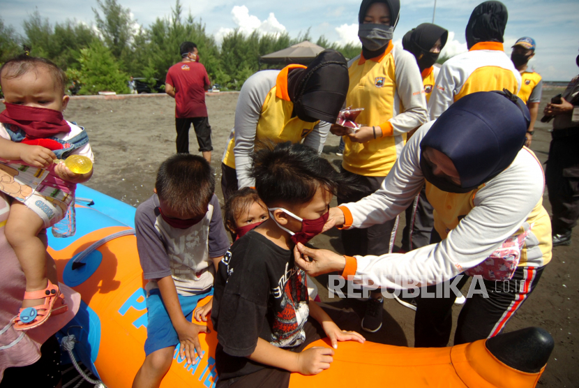Petugas kepolisian membantu anak-anak memakai masker di obyek wisata Pantai Alam Indah, Tegal, Jawa Tengah, Ahad (31/5/2020). Pemerintah daerah tersebut berencana membuka kembali tempat wisata pada 1 Juni 2020 dengan penerapan tatanan normal baru selama 30 hari mendatang