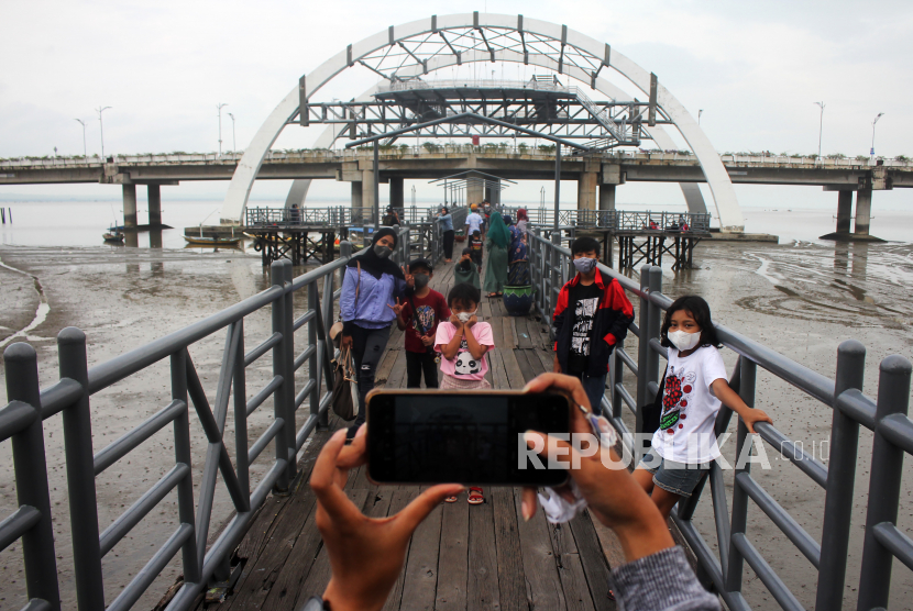 Pengunjung berswafoto dengan latar belakang Jembatan Suroboyo di Taman Hiburan Pantai Kenjeran, Surabaya, ilustrasi