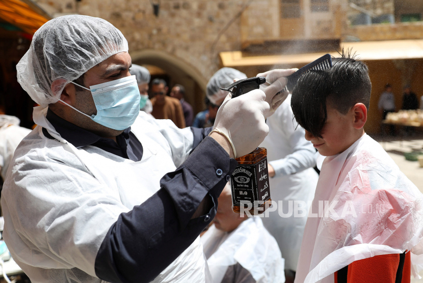 Penata rambut Palestina mengenakan masker kampanye potong rambut gtratis untuk warga Palestina di Tepi Barat, Hebron, Palestina, Senin (11/5). Pasalnya, saat pandemi virus corona Otoritas Palestina melarang penata rambut membuka gerai mereka