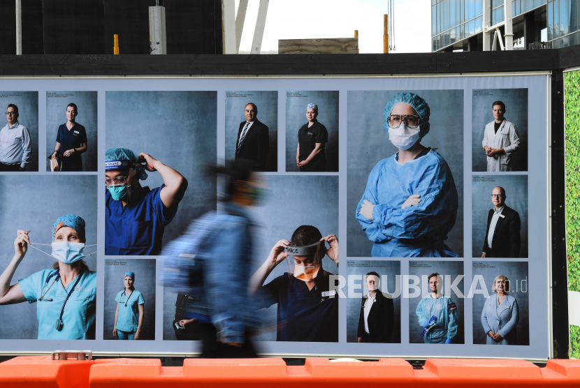 Pejalan kaki dengan memakai masker wajah melewati pameran fotografi luar ruangan tentang petugas kesehatan di Melbourne, Australia. Hingga Senin (28/9), lebih dari satu juta orang telah meninggal akibat Covid-19 di dunia.