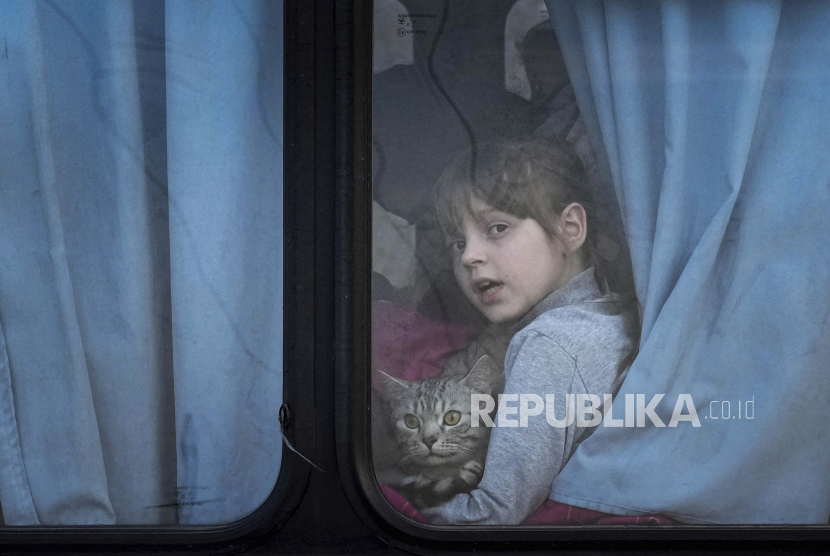 Seorang anak pengungsi internal yang memegang kucing peliharaan melihat keluar dari bus di pusat pengungsi di Zaporizhia, Ukraina, Jumat, 25 Maret 2022. 