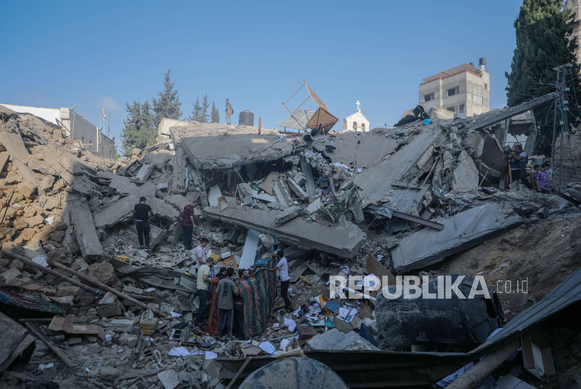 Orang-orang berdiri di antara puing-puing Gereja Ortodoks Yunani Saint Porphyrius menyusul serangan udara semalam di Gaza, 20 Oktober 2023. 