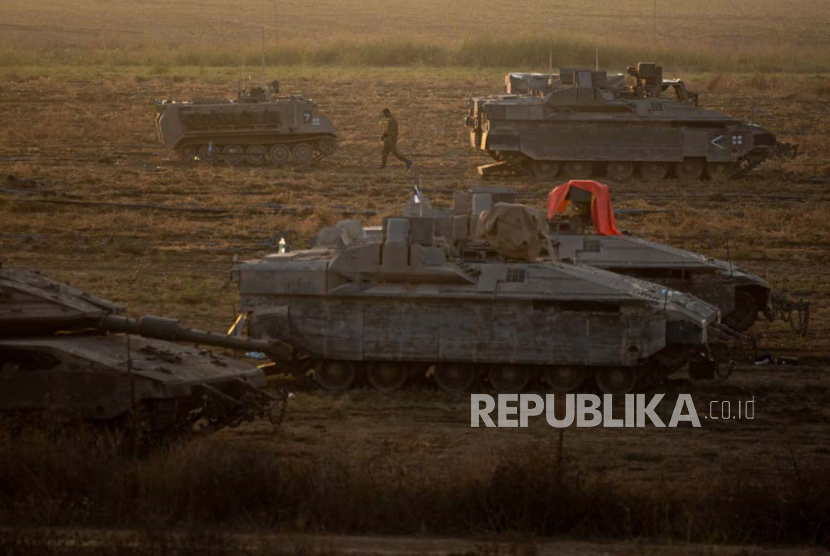 Seorang tentara Israel berjalan di samping kendaraan lapis baja yang duduk di daerah sepanjang perbatasan dengan Gaza, Israel selatan, 14 Oktober 2023.