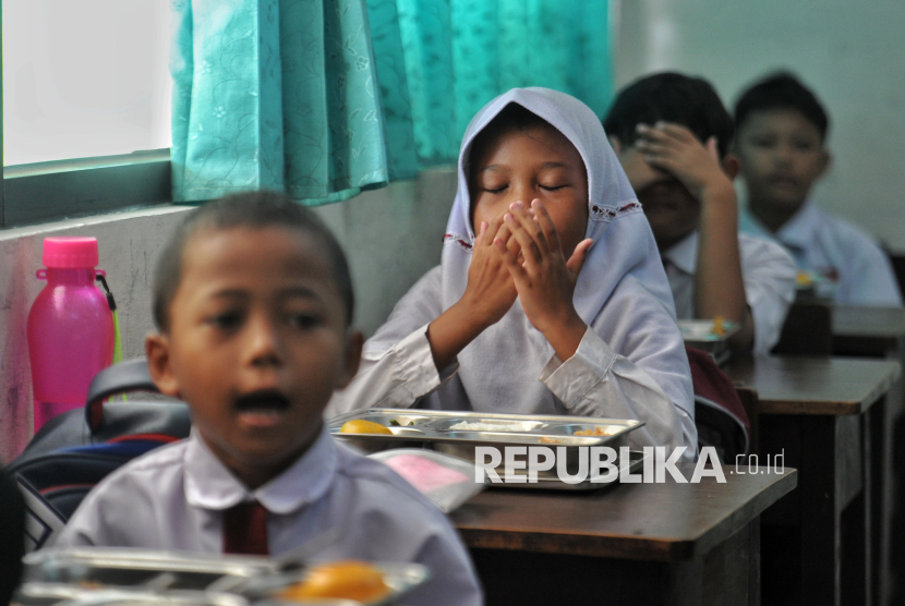 Siswa membaca doa sebelum menyantap Makanan Bergizi Gratis (MBG) di SDN 15 Slipi, Palmerah, Jakarta Barat, Senin (6/1/2025). Sebanyak 2.987 paket makanan bergizi didistribusikan kepada pelajar di sejumlah sekolah di wilayah Kecamatan Palmerah mulai dari tingkat Taman Kanak-kanak (TK) hingga Sekolah Menengah Pertama (SMP). Dalam satu paket makanan bergizi tersebut terdiri dari nasi putih, ayam goreng, sayur kacang panjang, tahu dan jeruk. Pada tahap awal program MBG ini, pemerintah mendistribusikan paket makanan di 190 titik di 26 provinsi mulai dari Aceh hingga Papua Selatan. Pada tahap awal Januari-Maret 2025, pemerintah menargetkan penerima manfaat dapat menyentuh tiga juta orang yang terdiri dari balita, santri, siswa PAUD, TK, SD, SMP, SMA, ibu hamil dan ibu menyusui. Jumlah tersebut akan terus bertambah hingga  mencapai 15 juta penerima manfaat pada akhir tahun 2025.