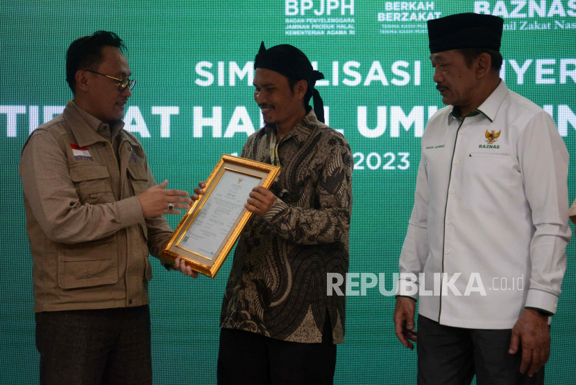 Kepala Badan Penyelenggara Jaminan Produk Halal (BPJPH) Kemenag Muhammad Aqil Irham (kiri) menyerahkan sertifikat halal kepada salah satu UMKM binaan Baznas RI disaksikan oleh Ketua Baznas RI KH Noor Achmad (kanan) pada acara simbolisasi penyerahan sertifikat halal UMKM binaan Baznas RI di Jakarta, Rabu (1/2/2023). Simbolisasi penyerahan sertifikat halal ini sebagai awal untuk mendorong serifikasi halal UMKM binaan Baznas dan LAZ di seluruh Idonesia. Acara penyerahan sertifikat halal tersebut dihadiri oleh 20 UMKM binaan Baznas RI yang bergeak di berbagai jenis usaha. 