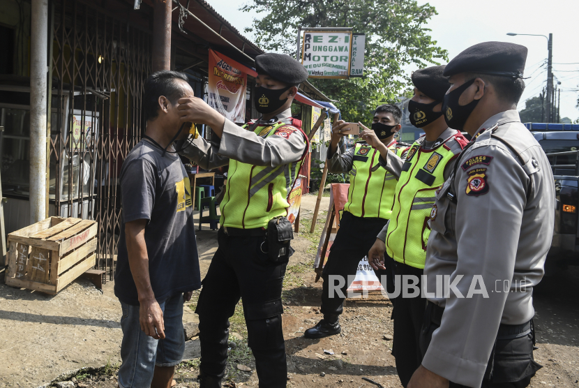 Petugas kepolisian memasangkan masker pada warga. Ilustrasi