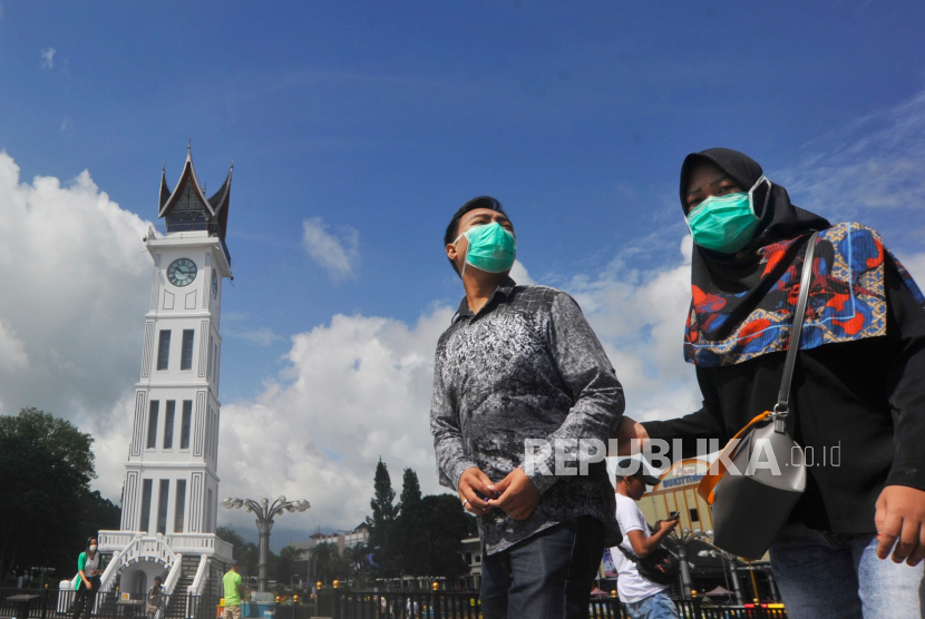 Pengunjung menggunakan masker melintas di depan Jam Gadang, Kota Bukittinggi, Sumatera Barat, Ahad (22/3). Kondisi dua warga Kota Bukittinggi, Sumatera Barat, yang dinyatakan positif coronavirus disease 2019 (Covid-19) berangsur membaik. Keduanya tengah menjalani perawatan di Rumah Sakit Achmad Mochtar (RSAM).