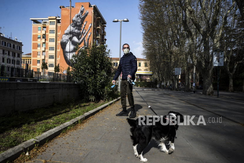 Seorang pria menggunakan masker wajah berjalan dengan anjingnya di lingkungan Trastevere saat lockdown darurat di Roma Italia, Ahad (29/3). Italia mendapat bantuan kiriman dokter dari Ukraina untuk mengatasi Covid-19.