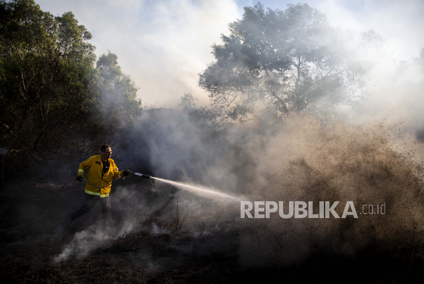 Seorang petugas pemadam kebakaran mencoba memadamkan api yang dimulai oleh perangkat pembakar yang diluncurkan dari Jalur Gaza.