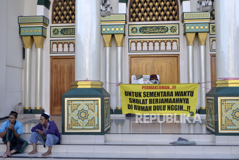 Dua orang warga duduk di dekat spanduk imbauan kepada jamaah untuk melaksanakan ibadah di rumah yang terpasang di Masjid Al-Muhajirin, Kepaon, Denpasar, Bali, Jumat (24/4). Seluruh masjid di wilayah Bali meniadakan aktivitas beribadah bagi para jamaah selama bulan Ramadhan sebagai salah satu upaya untuk mencegah penyebaran Covid-19.