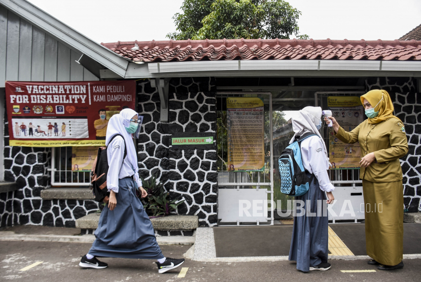 Guru memeriksa suhu tubuh siswa sebelum memasuki sekolah (ilustrasi).