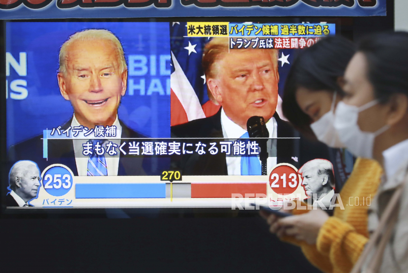  Orang-orang berjalan melewati layar TV yang menampilkan kandidat presiden dari Partai Demokrat dan mantan Wakil Presiden Joe Biden dan Presiden AS Donald Trump selama program berita yang melaporkan pemilihan presiden AS di Tokyo, Kamis, 5 November 2020.