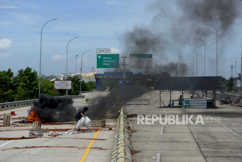 Warga membakar ban saat aksi penutupan akses jalan menuju Gerbang Tol Jatikarya 2 di Jalan Tol Cimanggis-Cibitung, Kota Bekasi, Jawa Barat, Rabu (8/2/2023). 