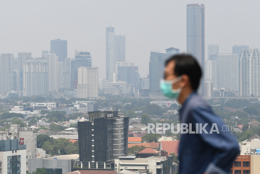 Warga mengenakan masker dengan latar belakang gedung-gedung bertingkat berselimut kabut asap di Jakarta, Kamis (25/8/2022). Lembaga data kualitas udara IQ Air pada Juli 2022 menempatkan Jakarta sebagai peringkat pertama dari sepuluh besar kota  paling berpolusi di Indonesia dengan indeks kualitas udara di angka 180 karena konsentrasi Particulate Matter (PM) 2.5 Jakarta berada pada angka 111.5 mikrogram per meter kubik atau 22,3 kali di atas nilai pedoman kualitas udara tahunan Badan Kesehatan Dunia (WHO). 