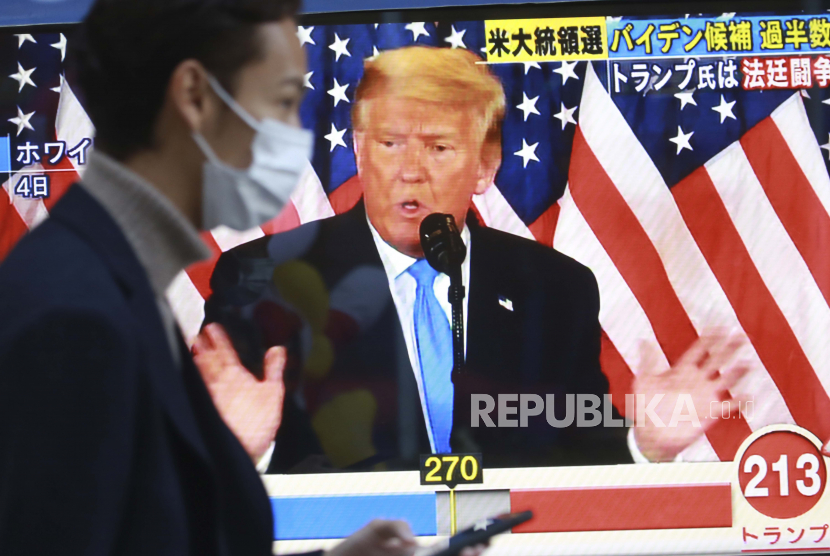  Seorang pria berjalan melewati layar TV yang menampilkan Presiden AS Donald Trump selama program berita yang melaporkan pemilihan presiden AS di Tokyo, Kamis, 5 November 2020.