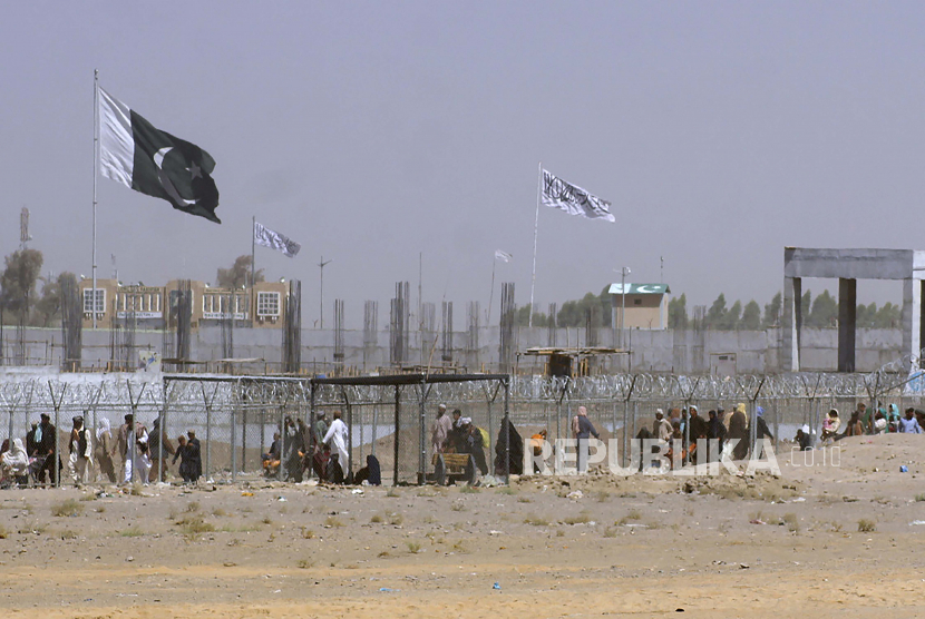 Bendera Pakistan dan Taliban berkibar di sisi masing-masing sementara orang-orang berjalan melalui penghalang keamanan untuk melintasi perbatasan di titik penyeberangan perbatasan antara Pakistan dan Afghanistan, di Chaman, Pakistan, Rabu, 18 Agustus 2021. Milisi Taliban di Pakistan menyatakan diakhirinya gencatan senjata selama sebulan. Ilustrasi.