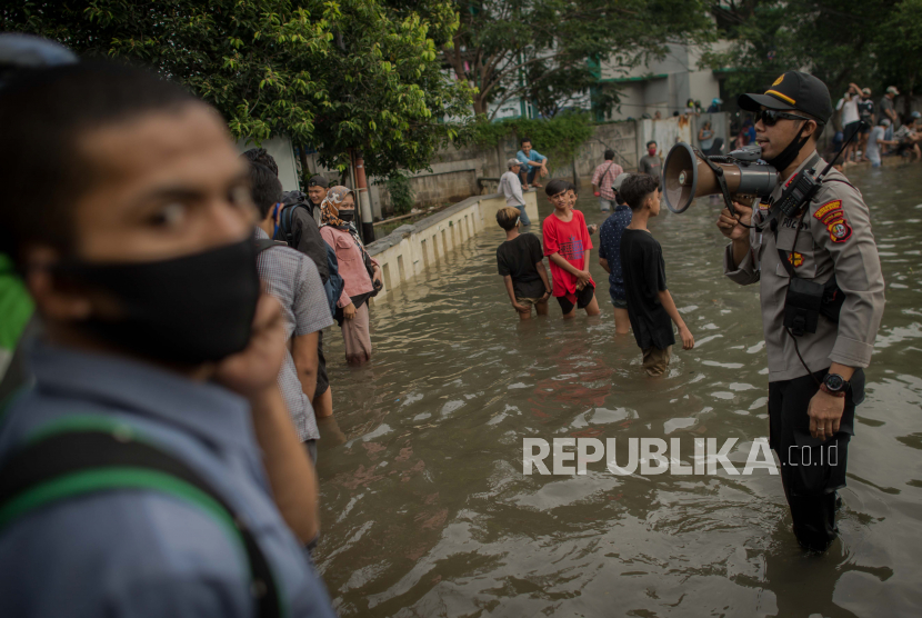 Petugas kepolisian mengatur lalu lintas serta mengimbau warga untuk menjaga jarak saat banjir di Jakarta Utara.