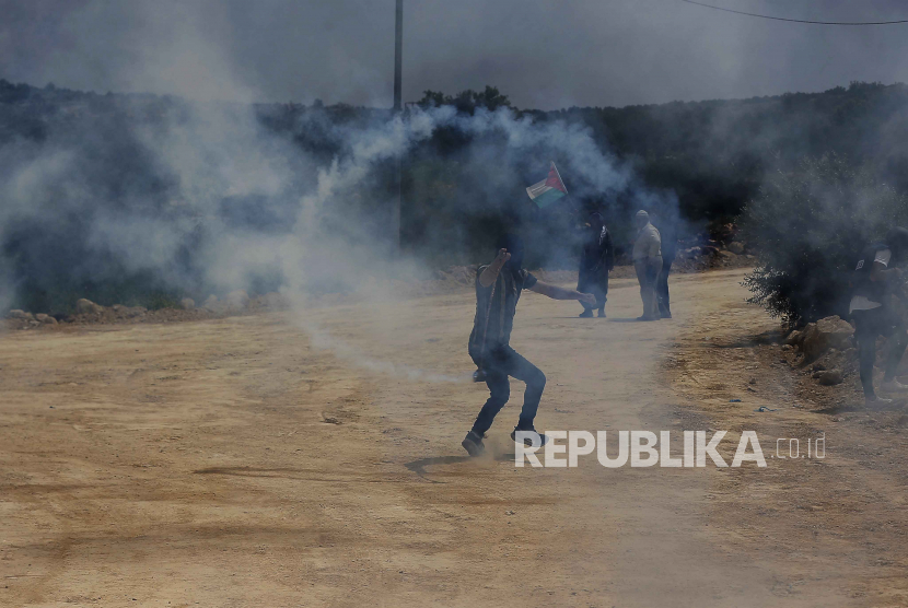 Seorang warga Palestina melempar granat gas air mata saat bentrokan dengan pasukan Israel setelah protes terhadap pemukim Israel  di Tepi Barat.