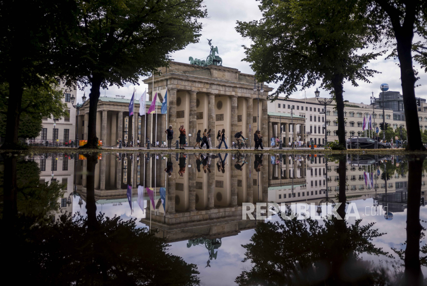Visitors who walk in front of the Brandenburg Gate are reflected reflecting in a puddle in Berlin, Germany, Thursday, June 29, 2023. 
