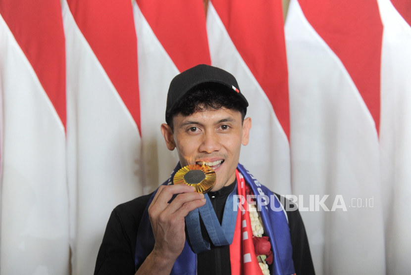 Atlet panjat tebing Indonesia Veddriq Leonardo berpose menggigit medali emas Olimpiade Paris 2024.