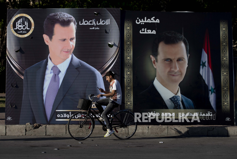  Seorang pria Suriah memeriksa ponselnya saat mengendarai sepedanya melewati poster kampanye Presiden Bashar Assad untuk pemilihan presiden mendatang yang menghiasi jalan di ibu kota Suriah, Damaskus,  Ahad (23/5).