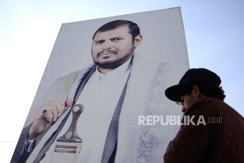 Seorang warga Yaman berjalan melewati spanduk besar yang menggambarkan pemimpin tertinggi Houthi, Abdul-Malik al-Houthi, di Sanaa, Yaman.