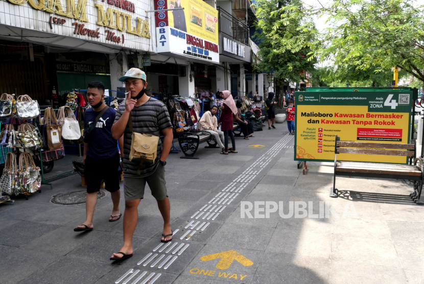 Pengunjung merokok di depan baliho tanda larangan rokok dan wajib masker di jalur pedestrian Malioboro. Pj Walkot Yogyakarta perbanyak tempat khusus merokok akibat marak perokok melanggar.