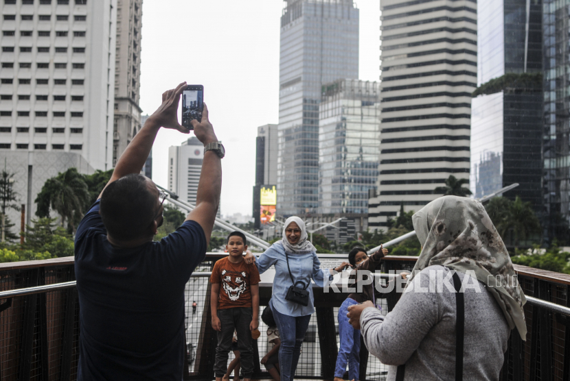 Sejumlah warga berfoto saat mengunjungi Jembatan Penyeberangan Orang dan Sepeda Pinisi di kawasan Sudirman, Jakarta, Ahad (3/4/2022). Jembatan penyeberangan yang menyajikan pemandangan lanskap gedung-gedung perkotaan tersebut menjadi salah satu destinasi alternatif untuk ngabuburit bagi masyarakat ibukota pada bulan Ramadhan 1443 Hijriah. Republika/Putra M. Akbar