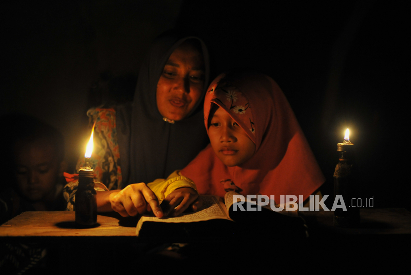 Seorang ibu mengajarkan anaknya mengaji dengan penerangan lampu minyak di Dusun Geragai, Desa Lagan Ulu, Tanjung Jabung Timur, Jambi, Ahad (9/7/2023). 