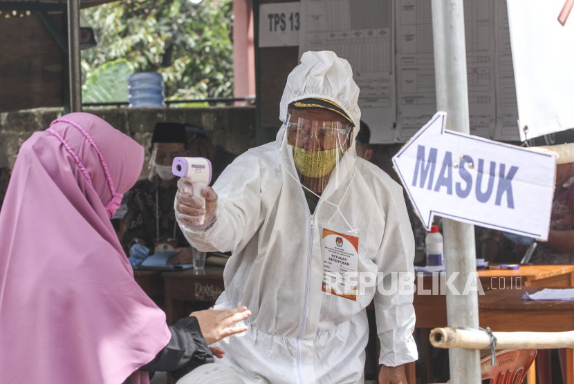 Petugas KPPS berpakaian baju hazmat dan alat pelindung diri (APD) mengukur suhu tubuh pemilih di Tempat Pemungutan Suara (TPS) 13, Cipayung, Depok, Jawa Barat, Rabu (9/12/2020). TPS di Kota Depok menerapkan protokol kesehatan pada Pilkada Serentak 2020 di masa Pandemi COVID-19. 