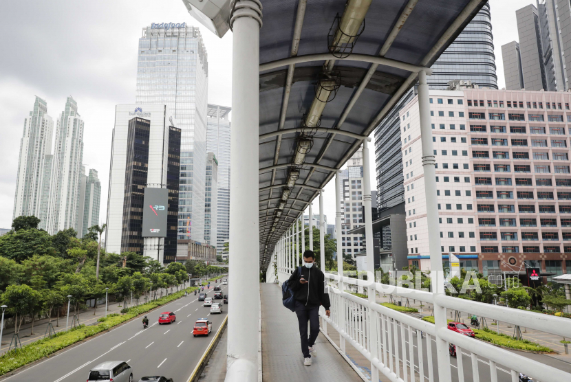 Seorang pria yang memakai masker pelindung wajah berjalan di jembatan penyeberangan di kawasan bisnis di Jakarta, Indonesia, 05 Januari 2021. Badan Pusat Statistik (BPS) menyatakan, pertumbuhan ekonomi Indonesia sepanjang tahun 2020 mengalami kontraksi dengan angka minus 2,07 persen.