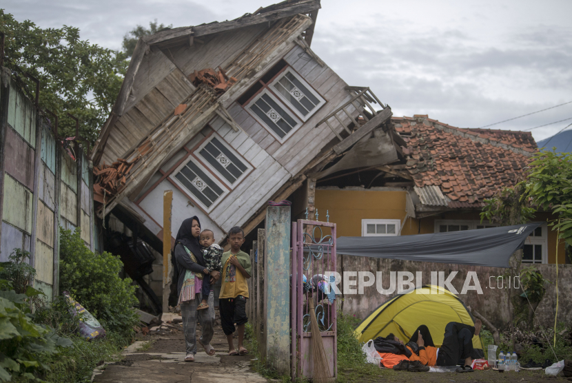 Seorang warga menggendong anaknya melintasi rumah yang rubuh akibat gempa bumi di Cieunder, Kabupaten Cianjur, Jawa Barat.