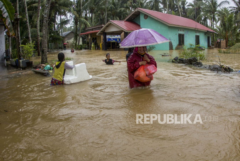 Warga melintasi banjir yang merendam salah satu kawasan permukiman di daerah Nongsa , Batam, Kepulauan Riau, Minggu (10/01/2021). Intensitas hujan yang cukup lebat mengakibatkan sejumlah pemukiman di Kota Batam tergenang banjir. 