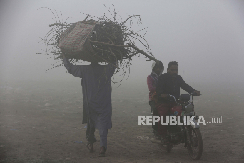 Seorang pria dan pengendara sepeda motor melintasi lapangan saat kabut tebal mengurangi jarak pandang, di Lahore, Pakistan, Selasa, 30 November 2021. Pakistan Revisi Aturan Karantina Penumpang Saat Kedatangan