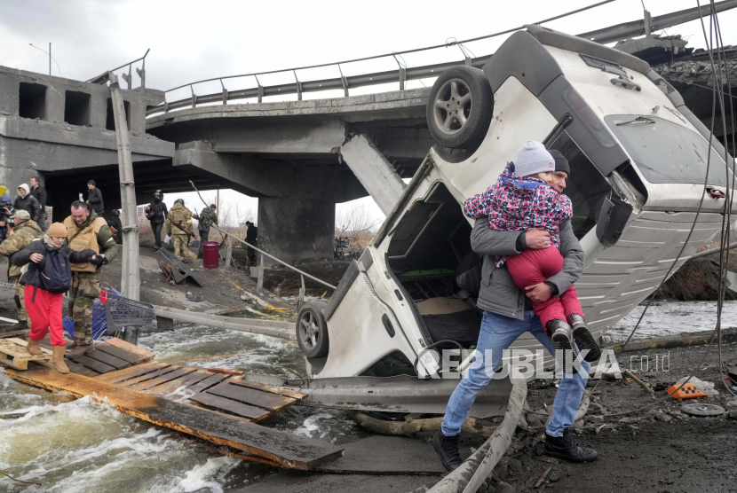 Orang-orang melintasi jalan darurat di bawah jembatan yang hancur saat melarikan diri dari kota Irpin dekat Kyiv, Ukraina, Senin, 7 Maret 2022.