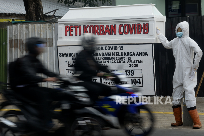 Pengendara sepeda motor melintas di samping replika peti mati dan  petugas yang mengunakan APD di Kawasan Kemang, Jakarta, Kamis (20/8). Pembuatan replika peti mati tersebut merupakan salah satu cara mensosialisasikan sekaligus memberi pesan moril kepada warga untuk menanati protokol kesehatan karena pandemi Covid-19 ini adalah virus berbahaya yang dapat menyebabkan kematian.Prayogi/Republika 