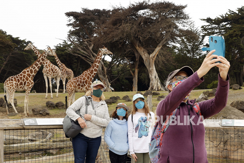  Sebuah keluarga mengambil selfie kelompok dengan jerapah selama pembukaan kembali Kebun Binatang & Kebun Binatang San Francisco, setelah hampir empat bulan penutupan karena pandemi coronavirus (COVID-19), di San Francisco, California, AS, 13 Juli 2020. Amerika Serikat (AS) telah mencatatkan delapan juta kasus Covid-19, Kamis (15/10).