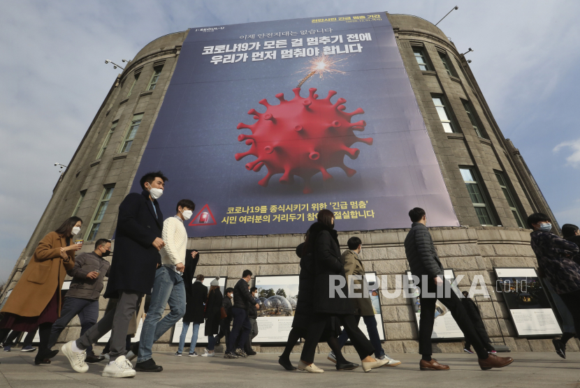  Orang-orang yang memakai masker wajah sebagai tindakan pencegahan terhadap virus corona berjalan di bawah spanduk yang menekankan kampanye jarak sosial yang ditingkatkan di depan Balai Kota Seoul di Seoul, Korea Selatan, Rabu, 25 November 2020.