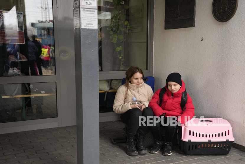  Dua orang, yang melarikan diri dari Ukraina, duduk di luar stasiun kereta dengan pembawa hewan peliharaan di Zahony, Hongaria, Senin, 7 Maret 2022. 