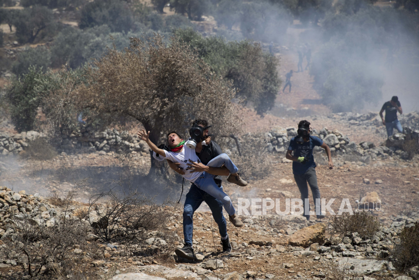Seorang pria Palestina membawa seorang anak laki-laki menjauh dari tabung gas air mata yang ditembakkan oleh tentara Israel selama protes terhadap pos terdepan pemukiman Yahudi Tepi Barat Eviatar yang dengan cepat didirikan bulan sebelumnya, di desa Palestina Beita, dekat kota Nablus, Tepi Barat, Jumat, 25 Juni 2021. 