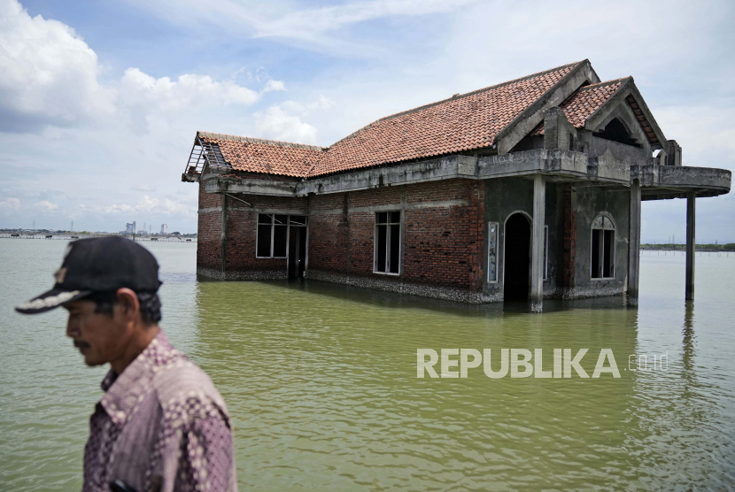 Seorang pria berjalan melewati sebuah rumah yang terbengkalai setelah terendam air akibat naiknya permukaan laut di Sidogemah, Jawa Tengah,  November 2021. 