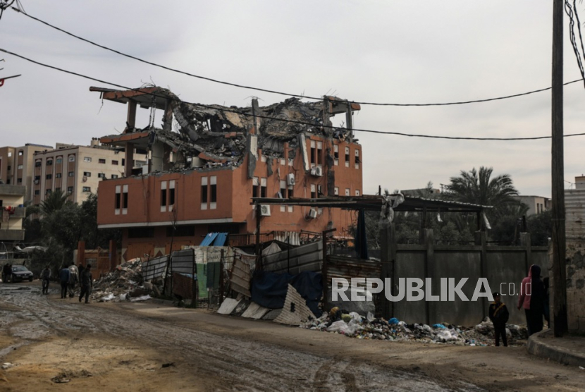 Orang-orang berjalan di dekat rumah yang hancur akibat serangan udara Israel di kota Deir Al Balah, Jalur Gaza selatan, 12 Februari 2024. 