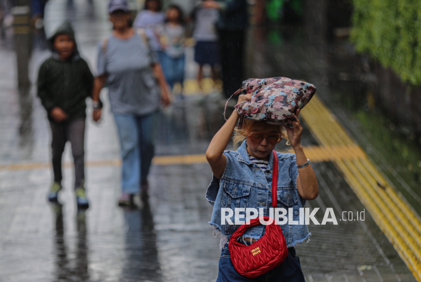 Warga menutupi kepalanya saat hujan di kawasan Bundaran Hotel Indonesia, Jakarta, Jumat (2/1/2026). Masyarakat kerap mengaitkan rambut basah kuyup akibat kehujanan atau yang dikenal dengan istilah keramas air hujan dengan berbagai gangguan kesehatan, mulai dari flu hingga sakit kepala.