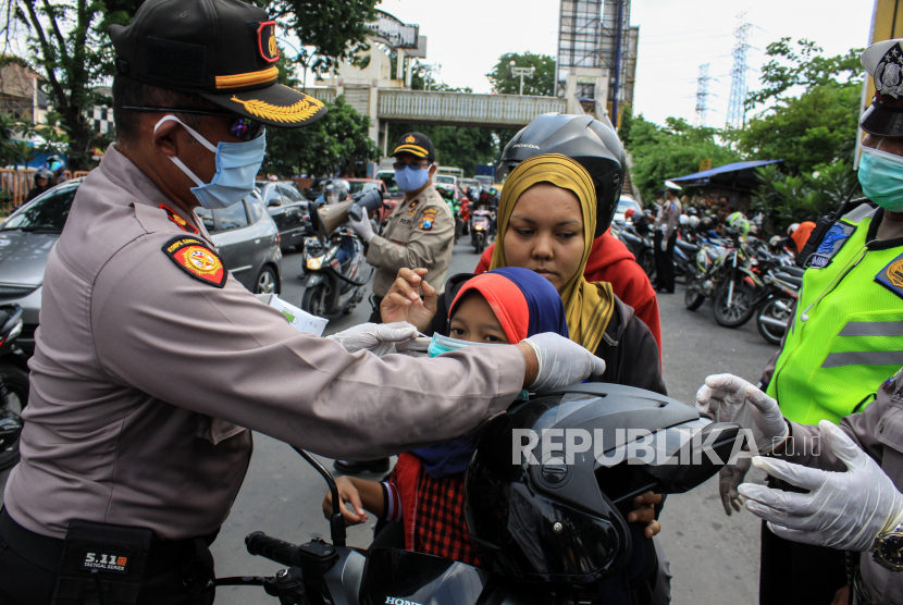 Petugas kepolisian membantu memasangkan masker kepada pengendara motor di depan Pos Polantas Waru, Sidoarjo, Jawa Timur, Rabu (15/4/2020). Selain mengimbau pencegahan wabah virus Corona (COVID-19), Satlantas Polresta Sidoarjo juga membagikan masker gratis kepada pengguna jalan yang tidak menggunakan masker agar terhindar dari virus Corona