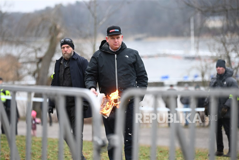 Pemimpin partai politik sayap kanan Denmark Stram Kurs, Rasmus Paludan, membakar sebuah mushaf Alquran, sambil diawasi oleh petugas polisi, saat dia melakukan protes di luar Kedutaan Besar Turki di Stockholm, Swedia, 21 Januari 2023.