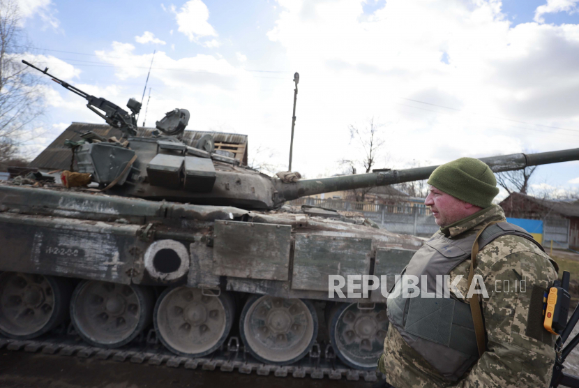 Seorang prajurit Ukraina berdiri di samping tank di desa Lukyanivka, wilayah Kyiv, Ukraina, Ahad, 27 Maret 2022.