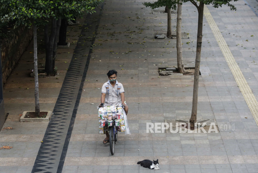 Seorang pedagang kaki lima mengendarai sepeda melewati seekor kucing di trotoar Jakarta