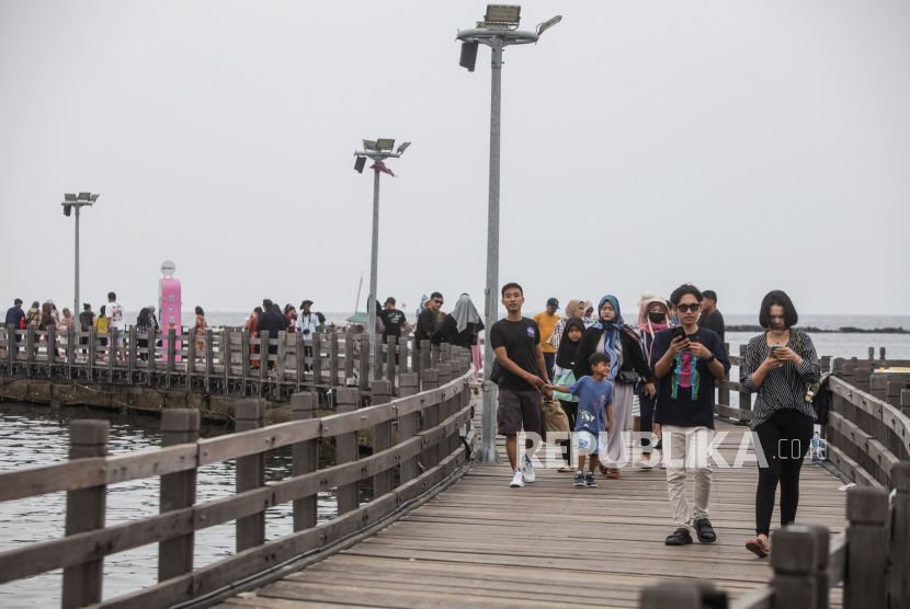 Sejumlah pengunjung berjalan melewati jembatan saat berwisata di Pantai Lagoon, Ancol, Jakarta.